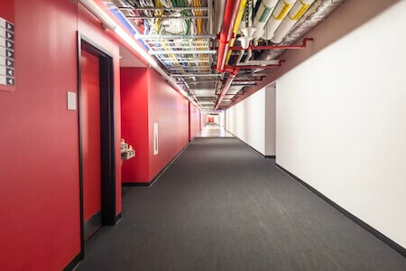 Vue d'un corridor avec plafond ouvert montrant les câbles et la tuyauterie dans un immeuble commercial
